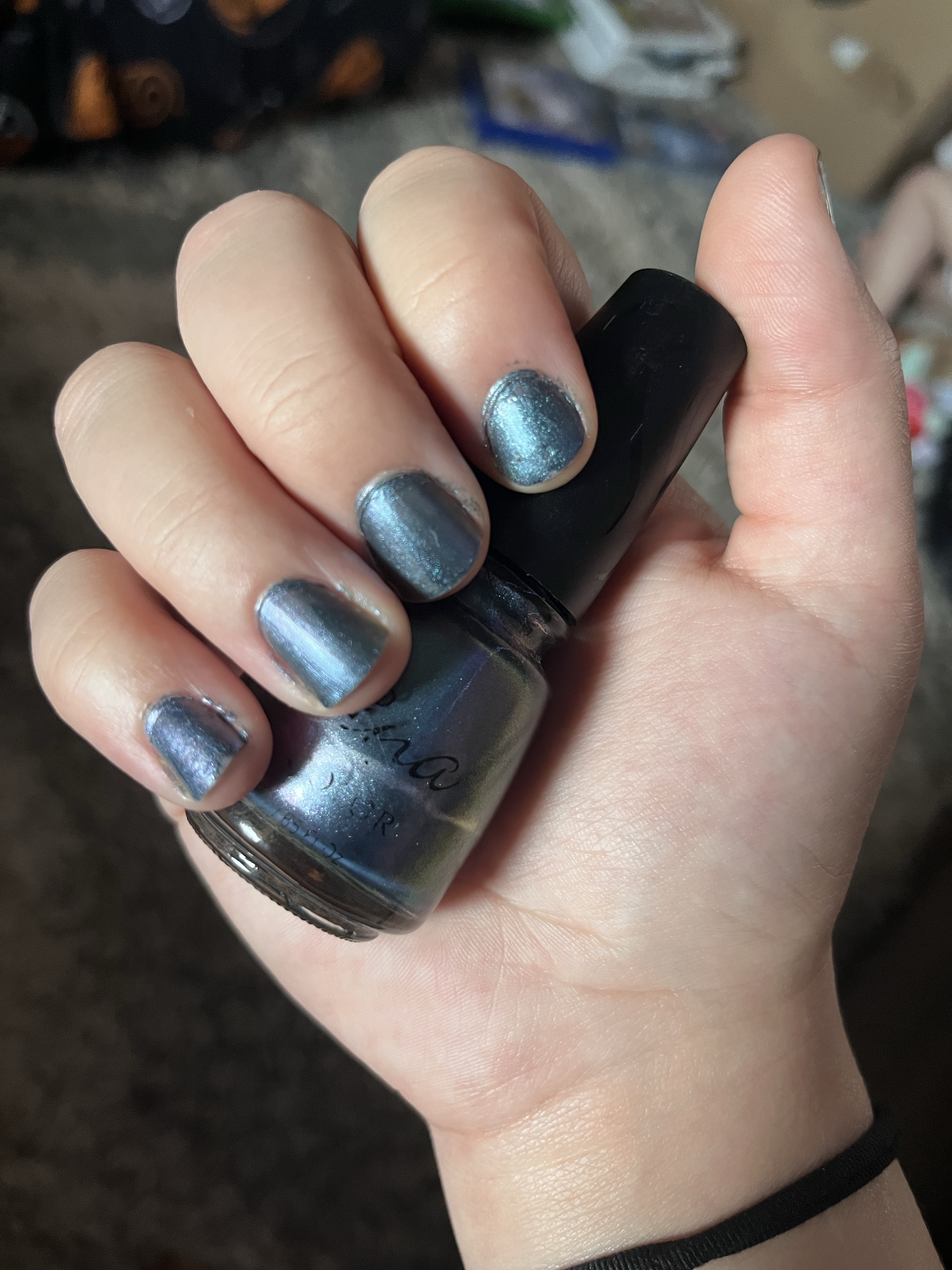 self-care act painting my nails. I chose a shimmery blue color and I am wearing a black hairtie around my wrist holding the nail polish bottle to show off my nails.